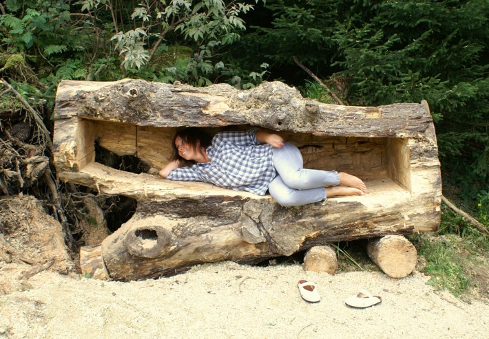 Eine Frau liegt in einem ausgehöhlten Baumstamm.